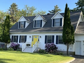 Stunning two-story home with a central entrance, flanked by windows and surrounded by a beautifully manicured lawn.