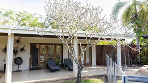 Ein modernes Haus mit überdachter Terrasse, kleinem Pool und Baum im Vordergrund.