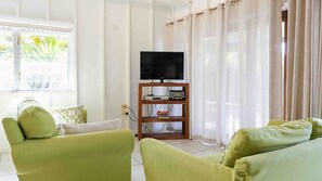 Ein Wohnzimmer mit Fernseher auf einem Holzboden, einer Couch und einem Fenster mit Vorhängen.