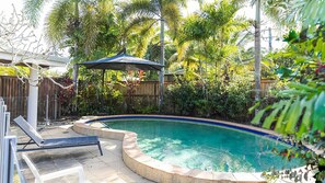 A swimming pool with a curved edge, surrounded by a wooden fence and lush greenery.