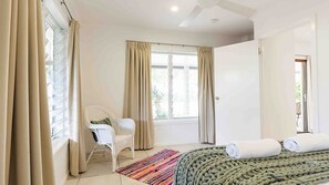 A bedroom with a bed, a chair, a window with curtains, and a view of greenery outside.
