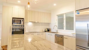 A modern kitchen with built-in appliances, a marble countertop, and a window.