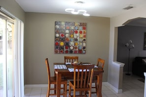 A dining area with a wooden table and chairs, a colorful abstract painting on the wall, and a ceiling light fixture.