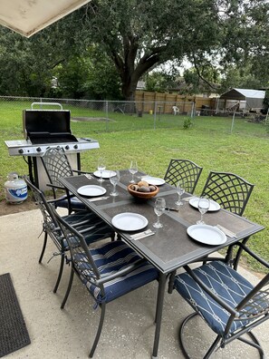 An outdoor dining area with a grill, metal chairs, and a table set for four. - 3/2 Modern Valrico Entire Home. Pet-Friendly! (Valrico)