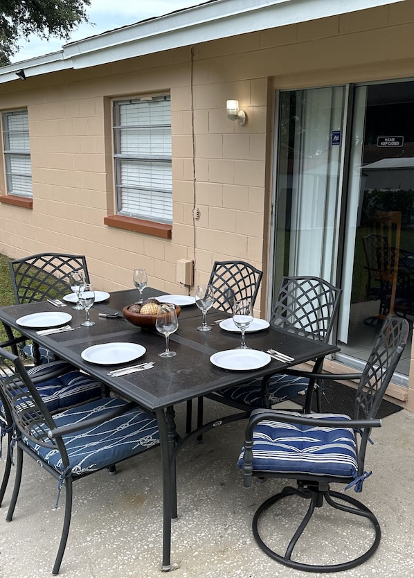 An outdoor dining area with a table set for six, surrounded by six chairs with blue cushions.