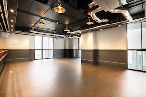A spacious, well-lit room with large windows, exposed ductwork, and a polished concrete floor.