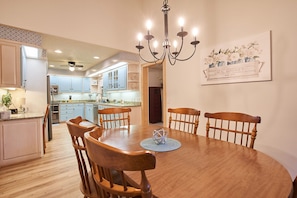 Uma sala de jantar com uma mesa redonda de madeira, seis cadeiras de madeira e um lustre.