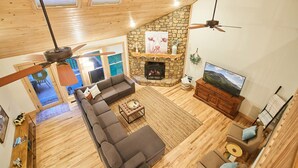 Un salon spacieux avec une cheminée en pierre, un plafond en bois et un grand téléviseur.