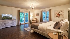 Une chambre avec un grand lit, une commode, une télévision et un balcon avec des rideaux.
