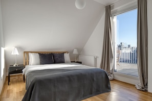 Una camera da letto con un letto, due comodini, una finestra con tende e vista sulla città.