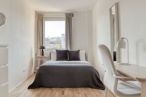 Quarto de hotel moderno com uma cama grande, uma escrivaninha, uma cadeira e uma janela com cortinas.
