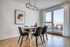 Uma área de jantar moderna com uma mesa redonda, seis cadeiras e uma grande janela com vista para uma varanda.