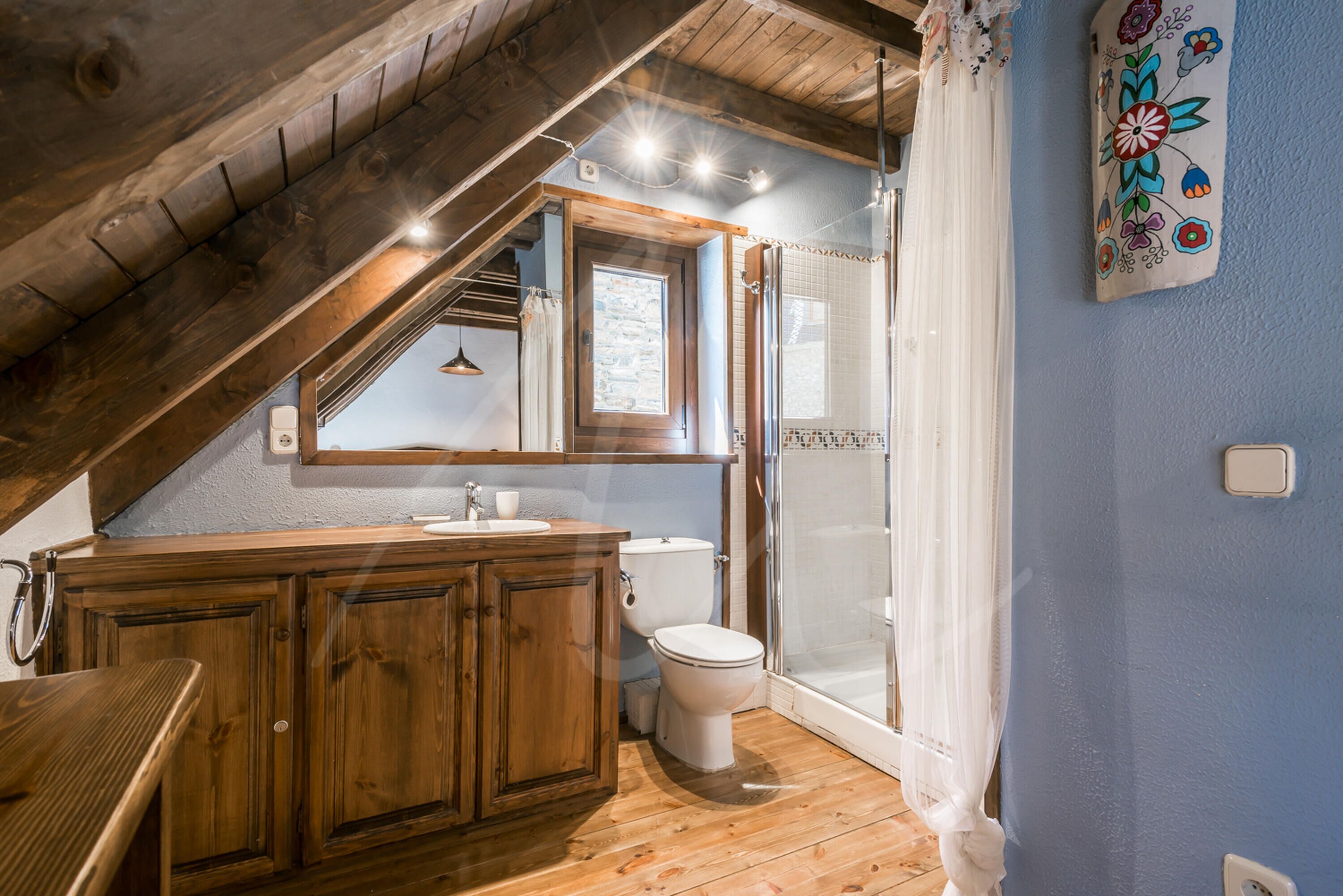 A bathroom with wooden cabinets, a sink, a toilet, and a glass shower enclosure.