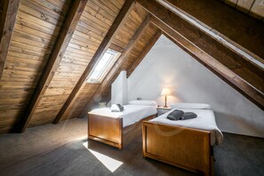 A small, cozy attic bedroom with two wooden beds, a skylight, and a nightstand with a lamp.