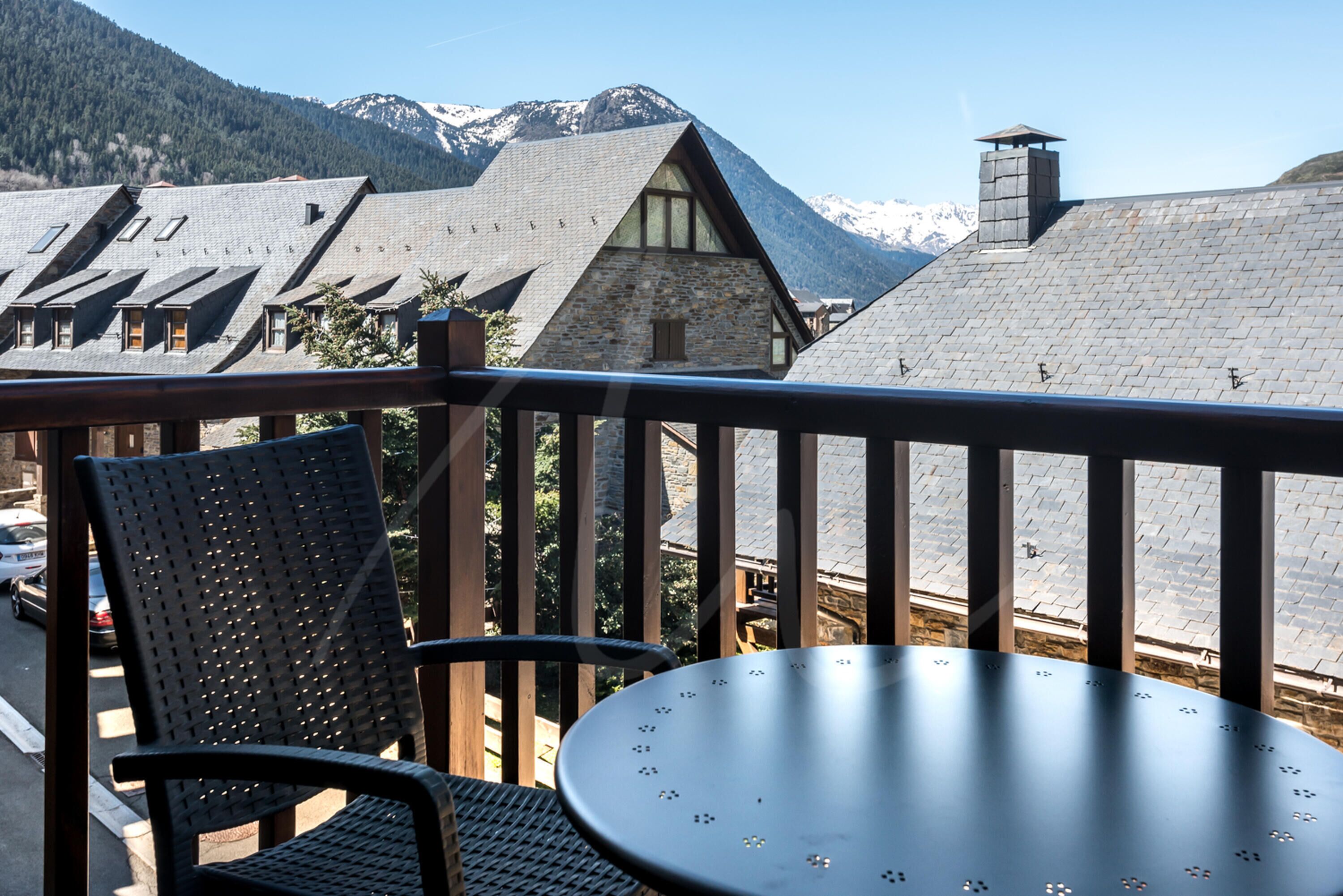 Un balcon avec une table et des chaises, donnant sur une chaîne de montagnes aux sommets enneigés.