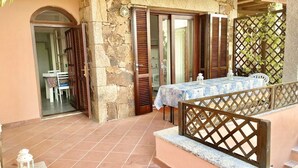 A stone-walled outdoor area with a table and chairs, a wooden fence, and a door leading to an interior space. - Nestled against a hill from which it takes its name, in one of the most prestigious areas of San Teodoro, lies the Citai apartment with sea view on Via Ticino, in a beautiful panoramic position.It is located on the ground floor with a garden or covered v (San Teodoro)