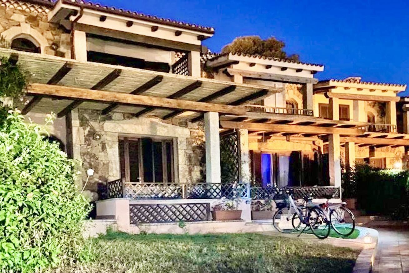 Un bâtiment traditionnel avec une façade en pierre, une pergola en bois et un vélo garé devant.