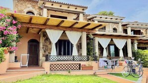 A two-story building with a stone facade, a wooden pergola over the entrance, and a small garden area with pink flowers. - Nestled against a hill from which it takes its name, in one of the most prestigious areas of San Teodoro, lies the Citai apartment with sea view on Via Ticino, in a beautiful panoramic position.It is located on the ground floor with a garden or covered v (San Teodoro)
