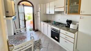 A compact kitchen with white cabinets, a gas stove, a refrigerator, and a dining area with a patterned tablecloth. - Nestled against a hill from which it takes its name, in one of the most prestigious areas of San Teodoro, lies the Citai apartment with sea view on Via Ticino, in a beautiful panoramic position.It is located on the ground floor with a garden or covered v (San Teodoro)