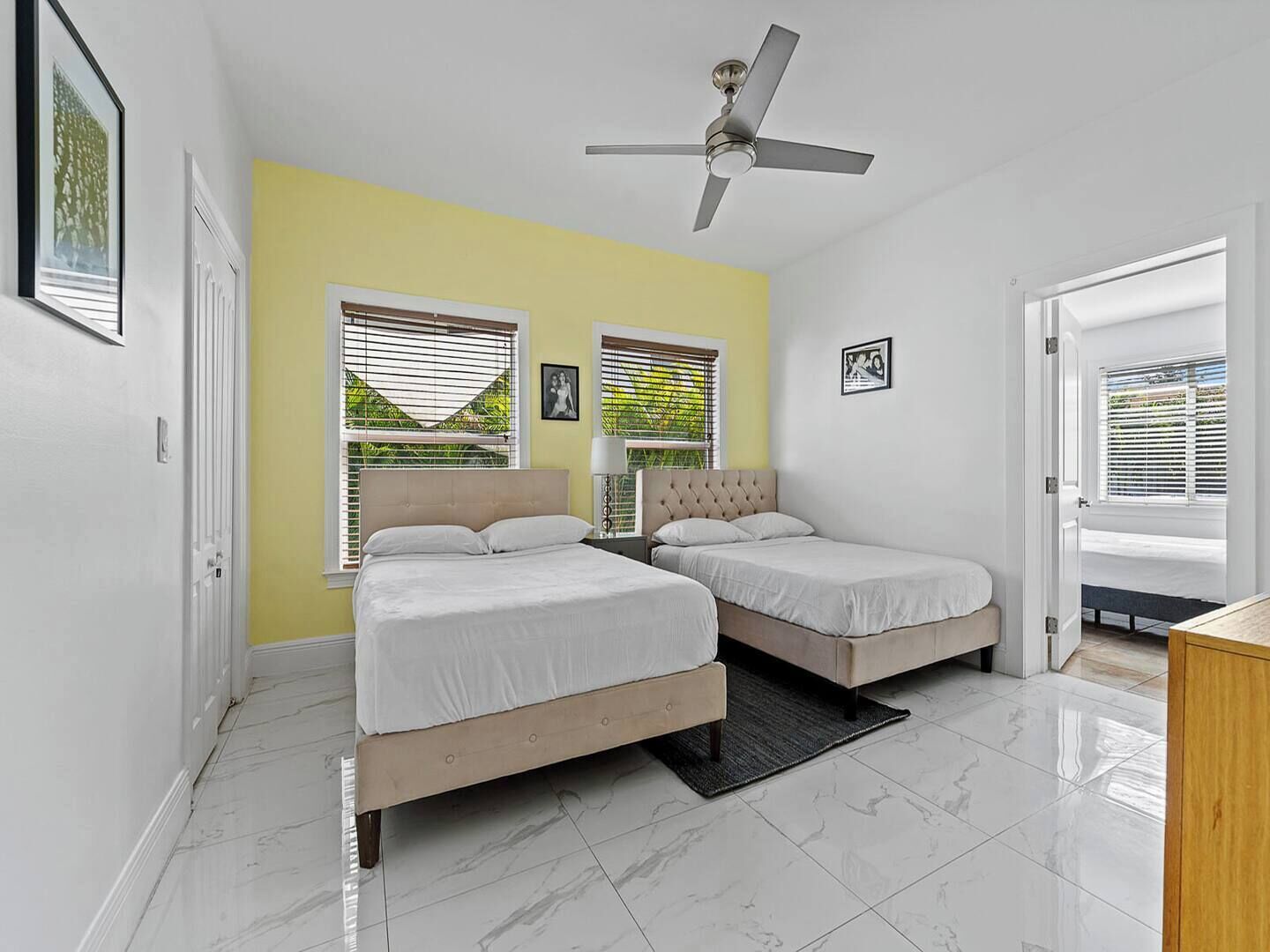 A bedroom with two beds, a ceiling fan, and large windows with blinds.