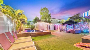 A backyard with a pool, lounge chairs, a covered seating area, and a small building.