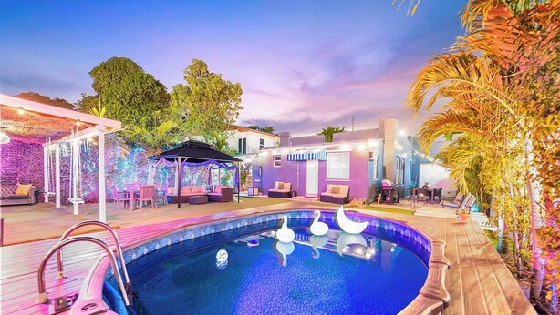 A swimming pool with a wooden deck, surrounded by outdoor seating and a covered area with string lights.