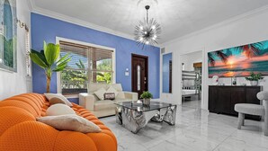 A modern living room with a blue accent wall, a large orange sofa, a glass coffee table, and a television displaying a sunset scene.