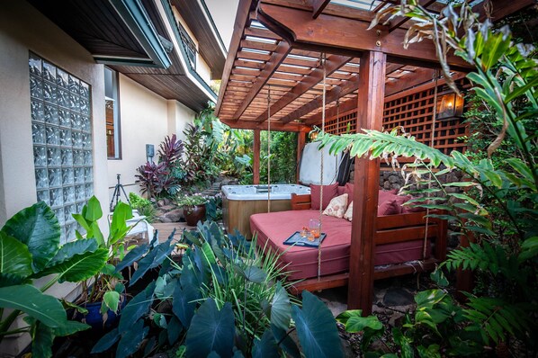 A cozy outdoor patio with a wooden swing, a hot tub, and lush tropical plants. - Tropical Rendezvous Suite - Luxury Studio in tropical gardens with koi ponds. (Koloa)