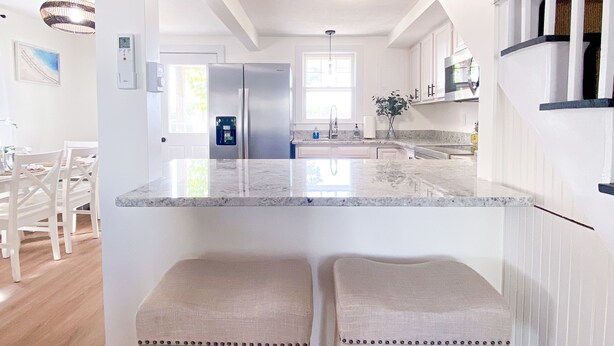 Una cocina moderna con una isla central, dos taburetes, un refrigerador y un comedor con sillas.