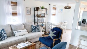 Una sala de estar con un sofá, un sillón azul, una mesita de centro y una estantería.