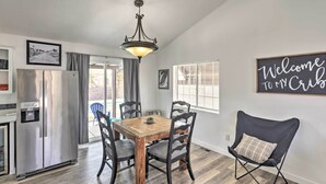A dining area with a wooden table and chairs, a black chair with a cushion, a refrigerator, and a 'Welcome to My Cabin' sign.