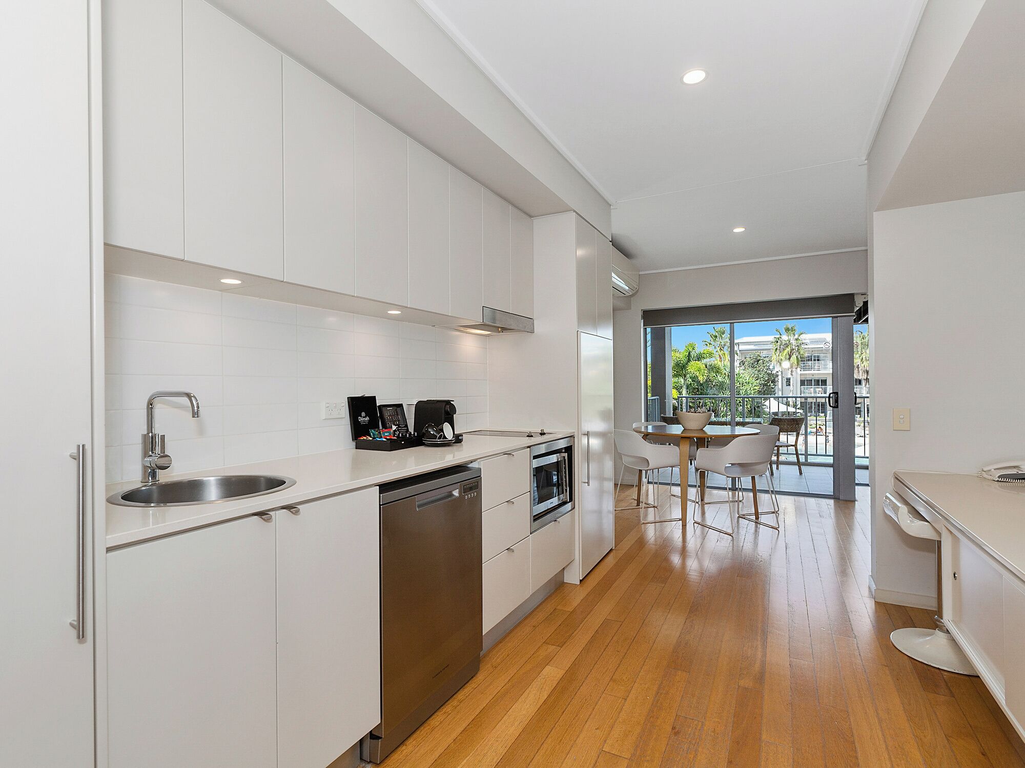 A modern kitchen with white cabinets, stainless steel appliances, and a wooden floor.