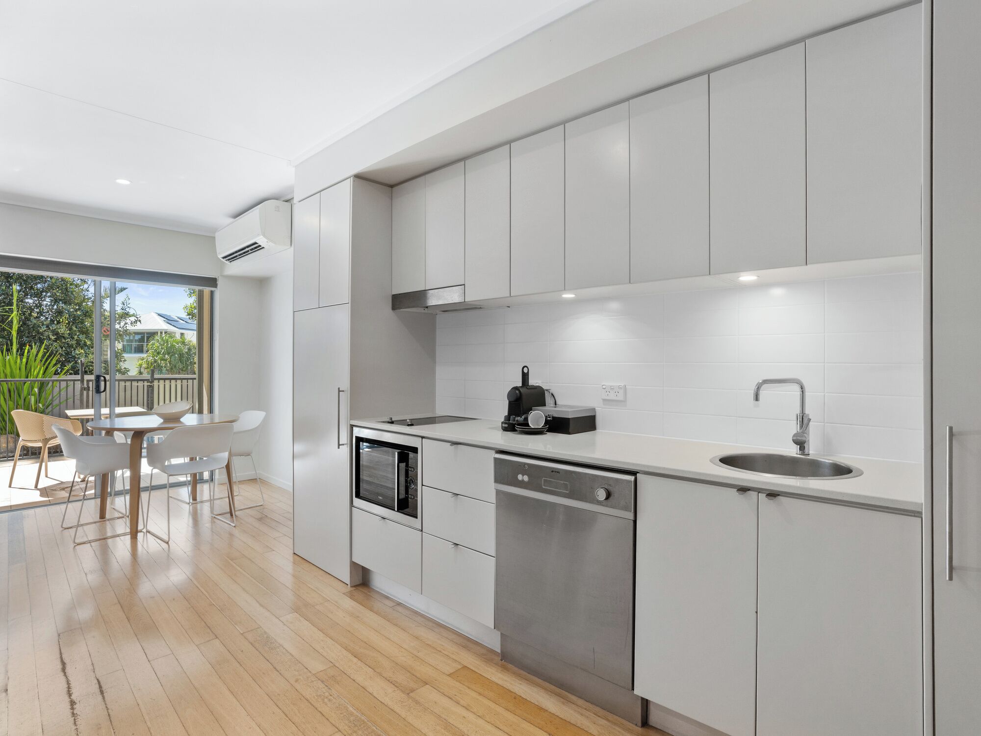A modern kitchen with white cabinets, stainless steel appliances, and a large window overlooking a balcony.