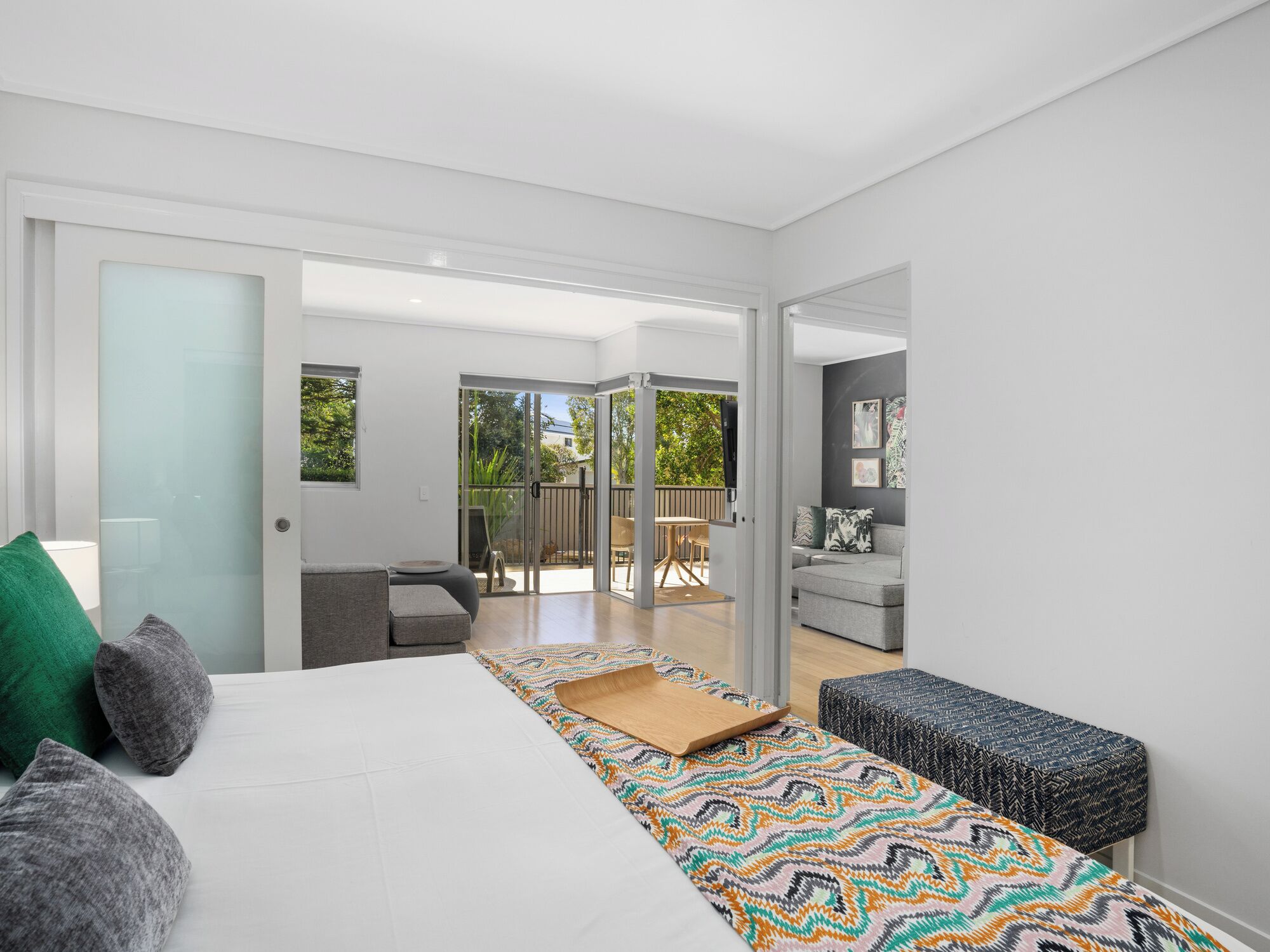 Ein modernes Schlafzimmer mit einem großen Bett, einem kleinen Sofa, einer Bank und einer Schiebetür zu einer Außenpatio.