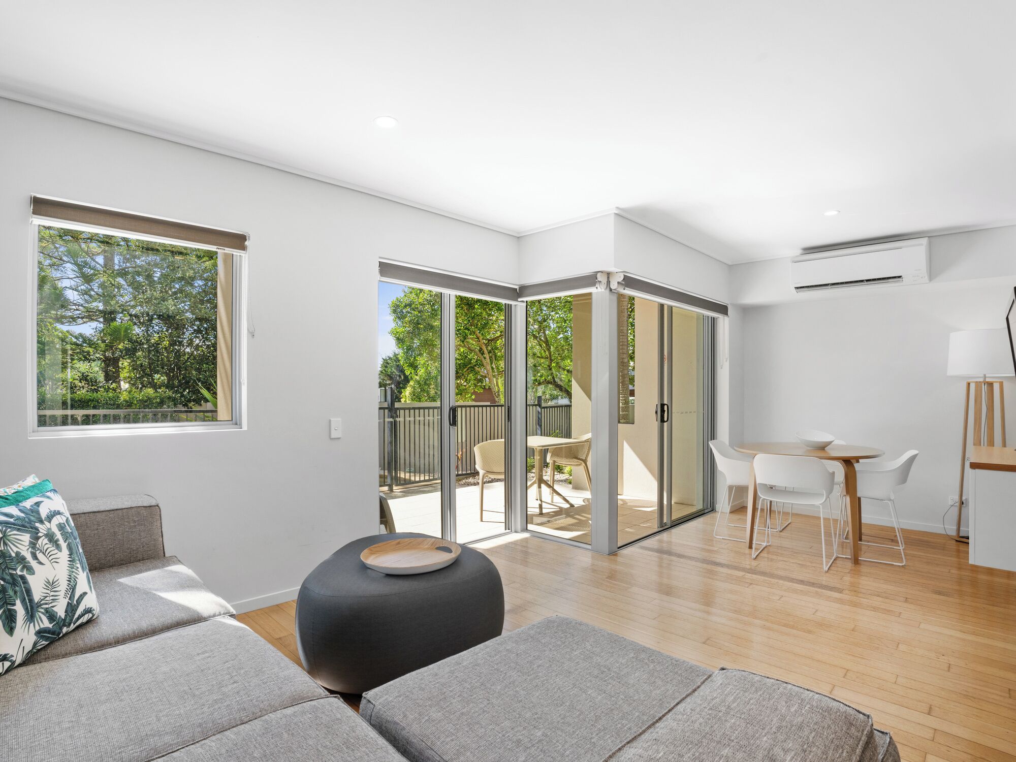 Una sala moderna con un sofá, un reposapiés y una zona de comedor con sillas y una mesa.