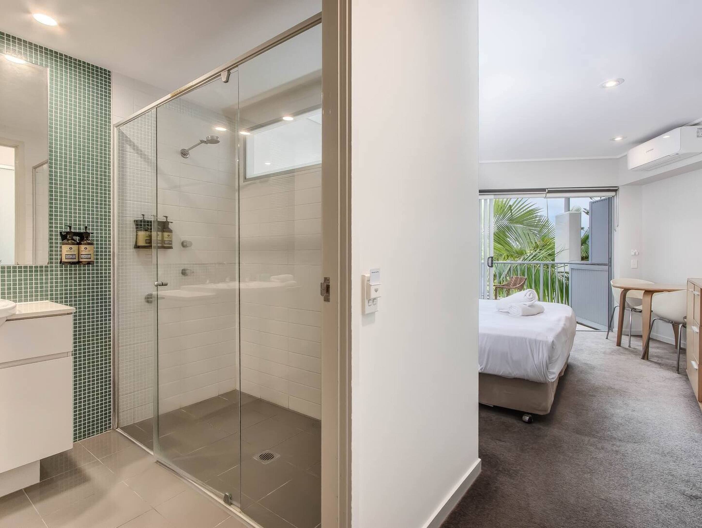 A modern bathroom with a glass-enclosed shower, a white sink, and a green-tiled wall.