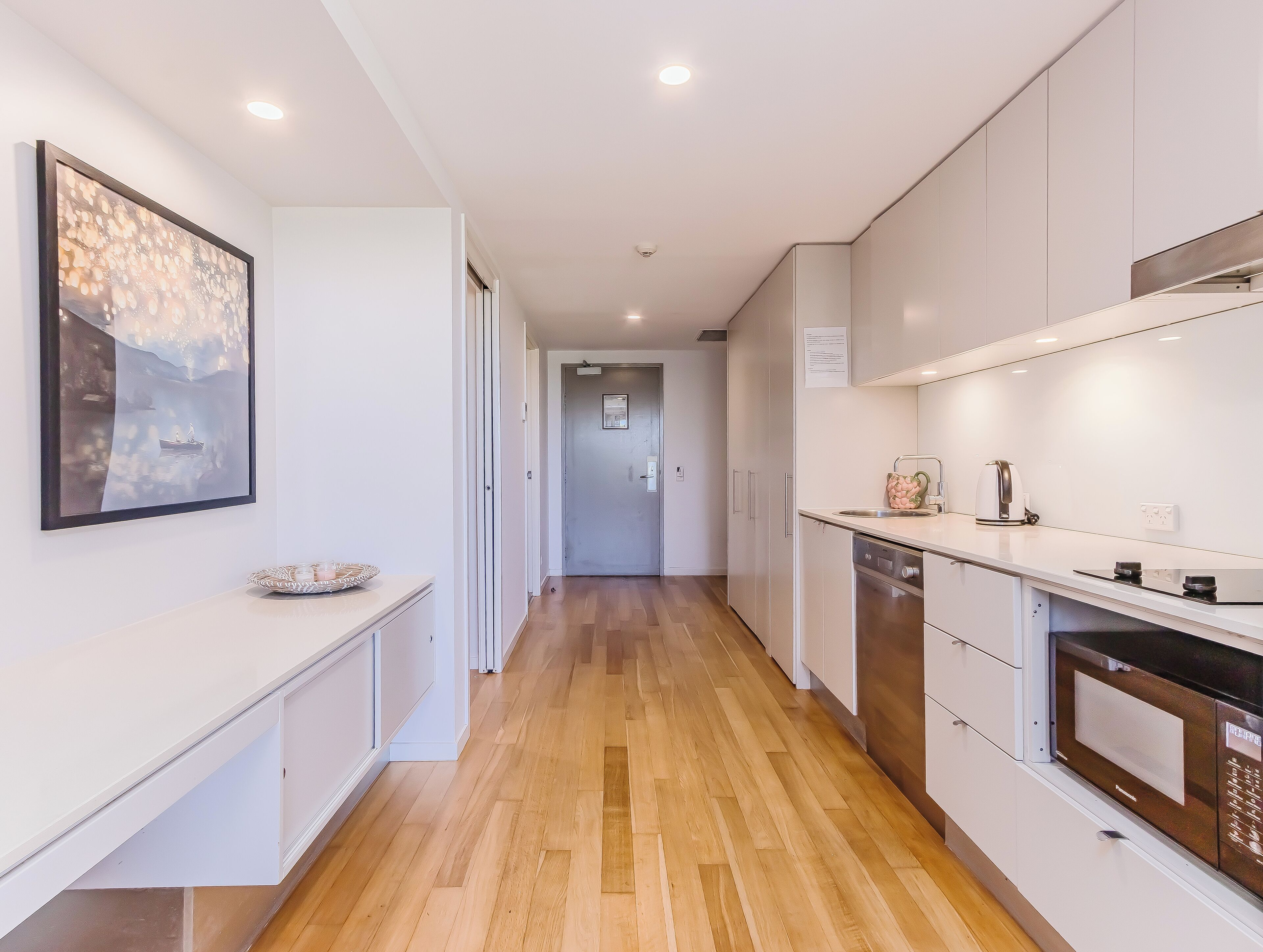 A modern kitchen with white cabinets, a wooden floor, and a painting on the wall.