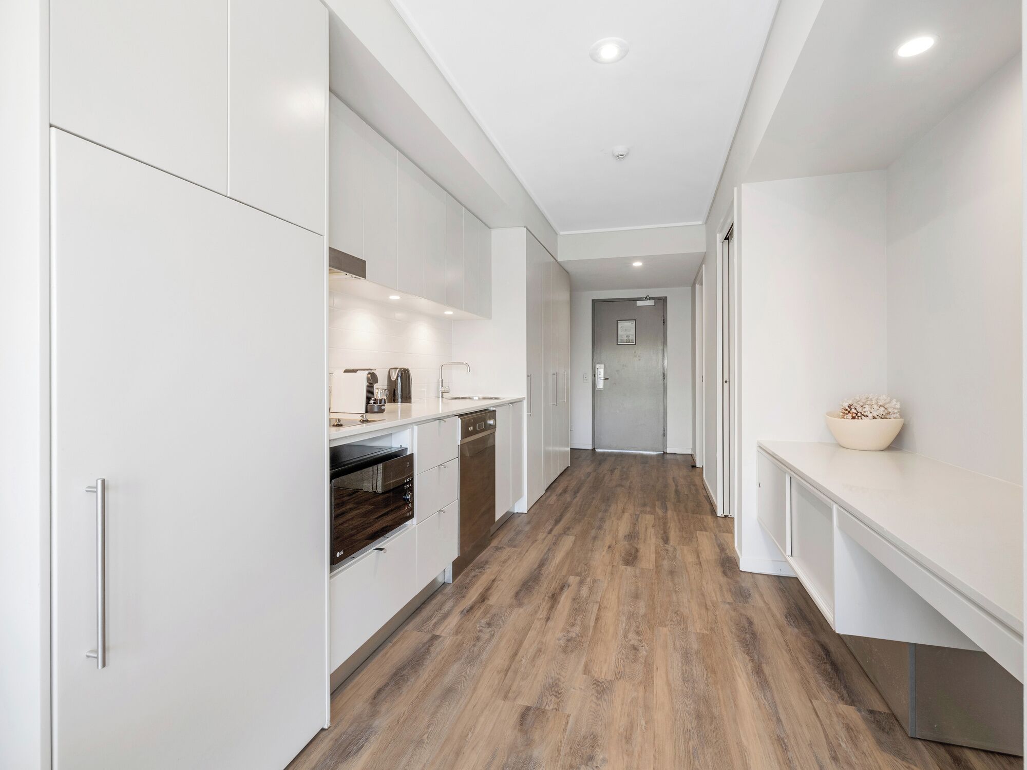 A modern kitchen with white cabinetry, a wooden floor, and a recessed ceiling light.