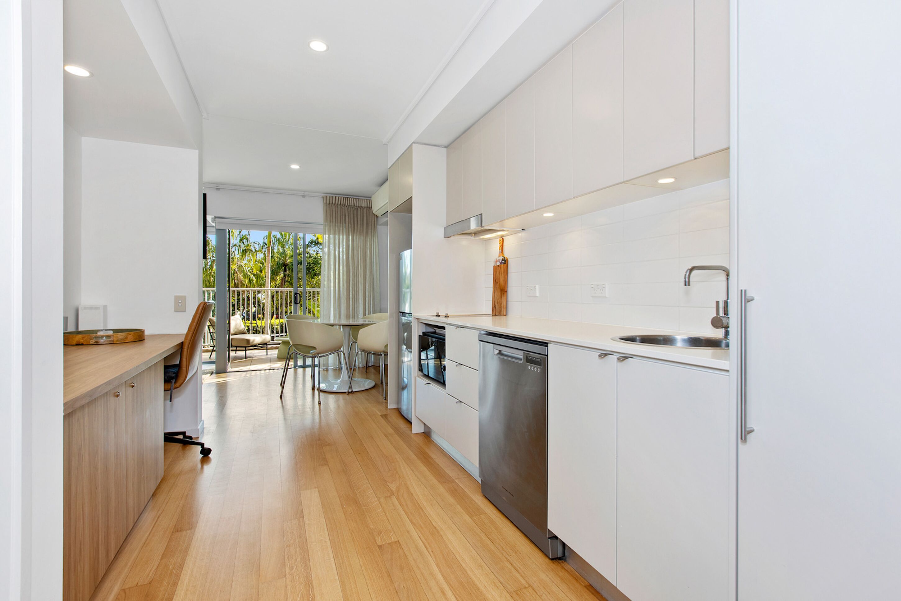 Una cocina moderna con armarios blancos, electrodomésticos de acero inoxidable y una mesa de madera con sillas.