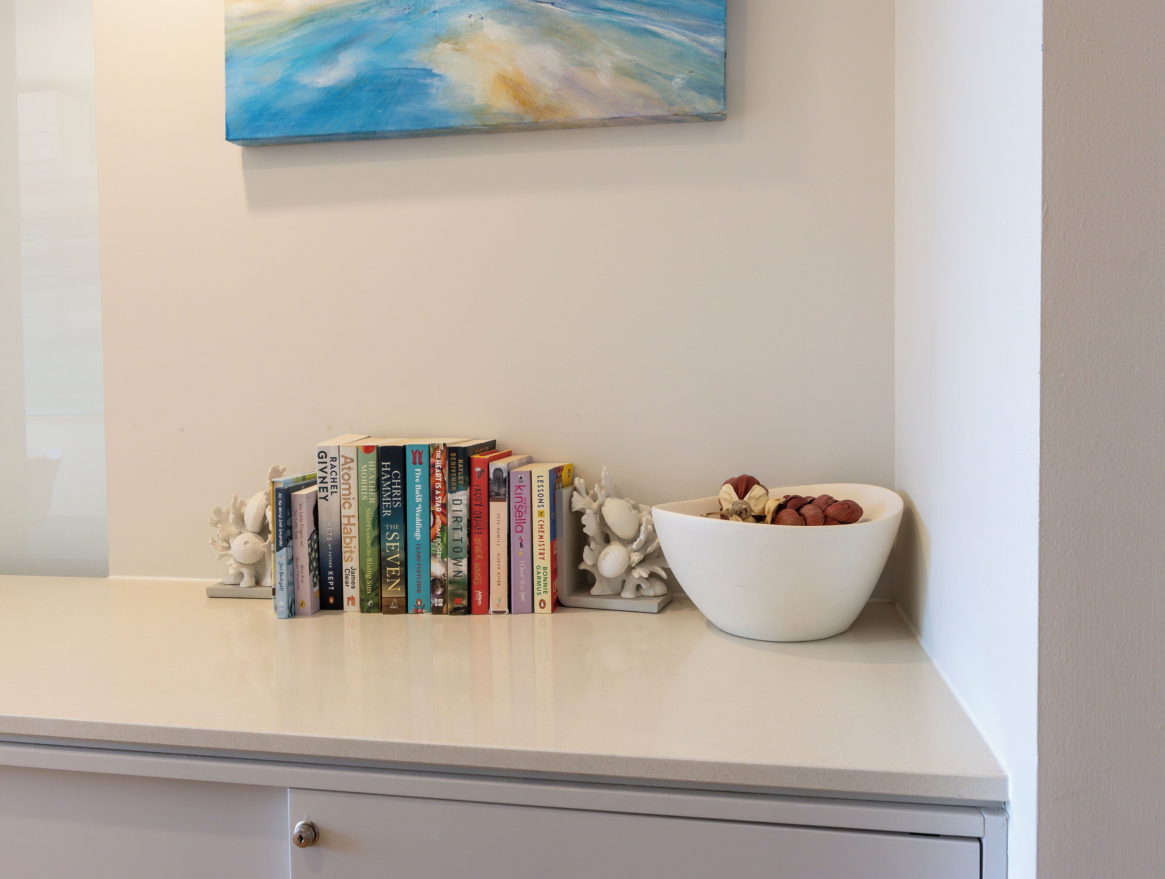 A white desk with a row of books, a white bowl with nuts, and a decorative plant.