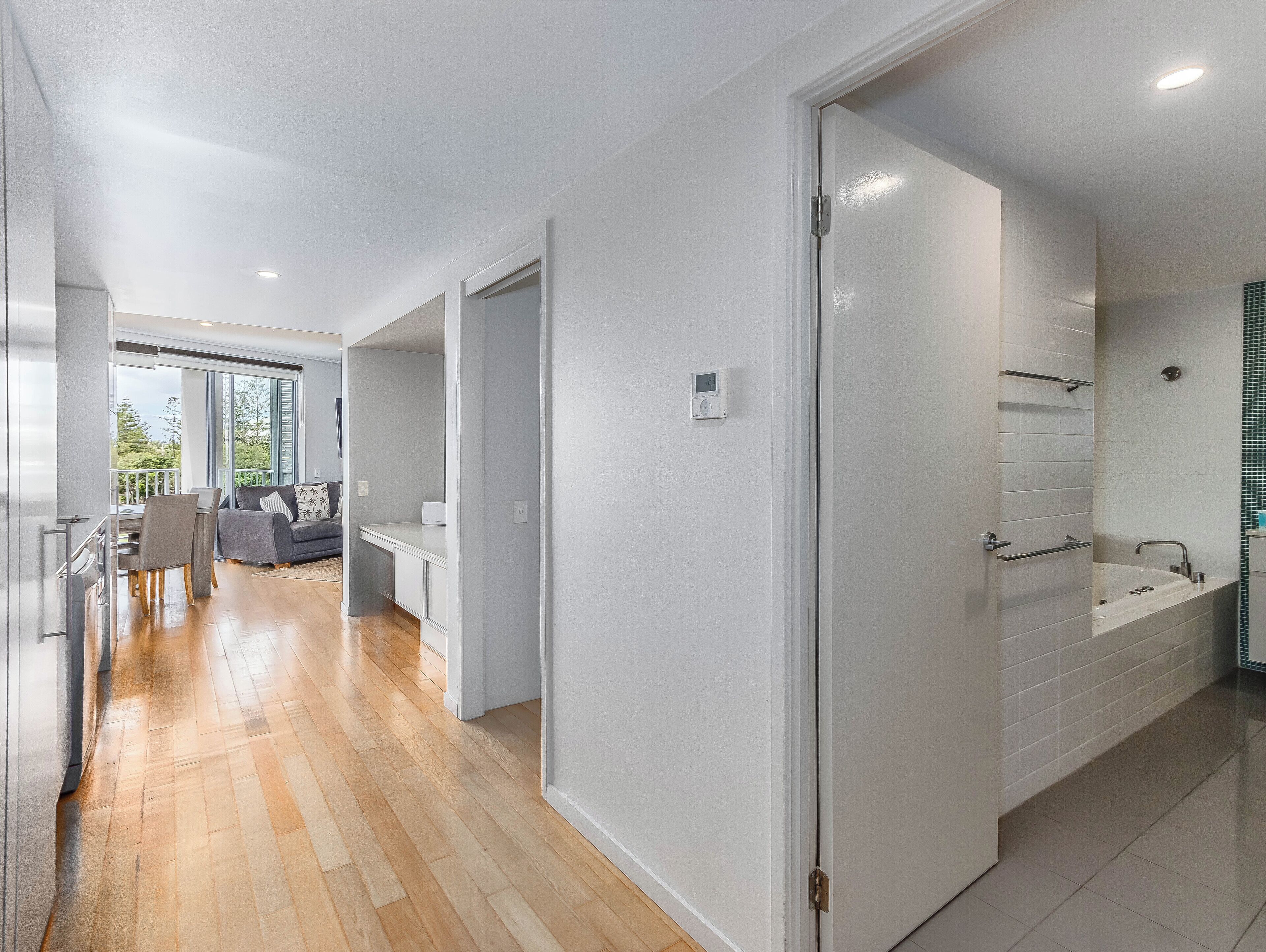 A modern interior with a wooden floor, a dining area with chairs and a table, a sofa, and a bathroom with a bathtub and tiled walls.