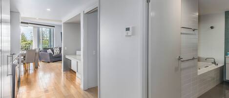 A modern interior with a wooden floor, a dining area with chairs and a table, a sofa, and a bathroom with a bathtub and tiled walls.