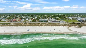 An aerial view of a coastal town with a beach, buildings, and greenery.