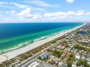 An aerial view of a coastal town with a beach, houses, and a road.
