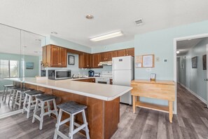 A modern kitchen with a central island, bar stools, wooden cabinets, and a refrigerator.