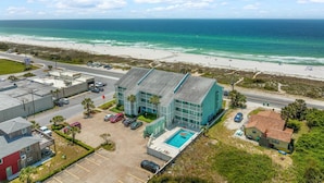 A coastal hotel with a swimming pool, beach view, and parking area.