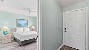 A bedroom with a bed, nightstands, a ceiling fan, and a door.