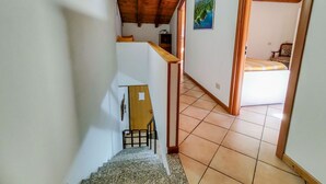 Eine Treppe führt zu einem Schlafzimmer mit einem Bett, einem Bild an der Wand und einer Holzbalkendecke.