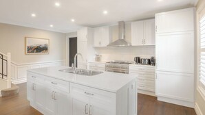 A modern kitchen with white cabinetry, a central island with a sink, a stove, and a range hood.