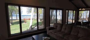 A living room with large windows, a sofa, and a view of a grassy area and trees. - Waterfront, Panoramic Views! White Star Point (Brussels)